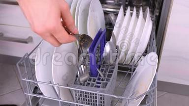 男人`手在洗碗机里放<strong>一个</strong>白色的脏盘子和<strong>勺子</strong>，然后在厨房里运行。